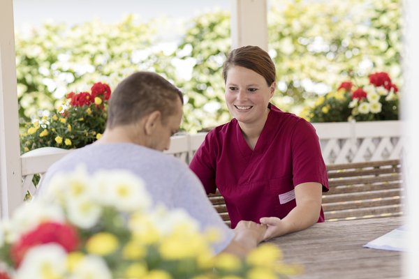 Eine Hospizmitarbeiterin spricht im Freien mit einem Bewohner.
